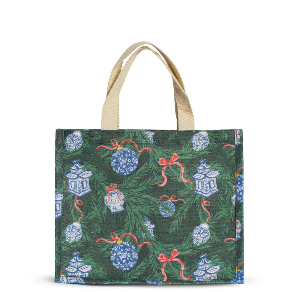 A canvas tote bag featuring a festive Christmas tree print with green pine branches, blue-and-white porcelain ornaments, red bows, and blue lantern motifs, complete with natural beige shoulder straps, shown against a plain white background.