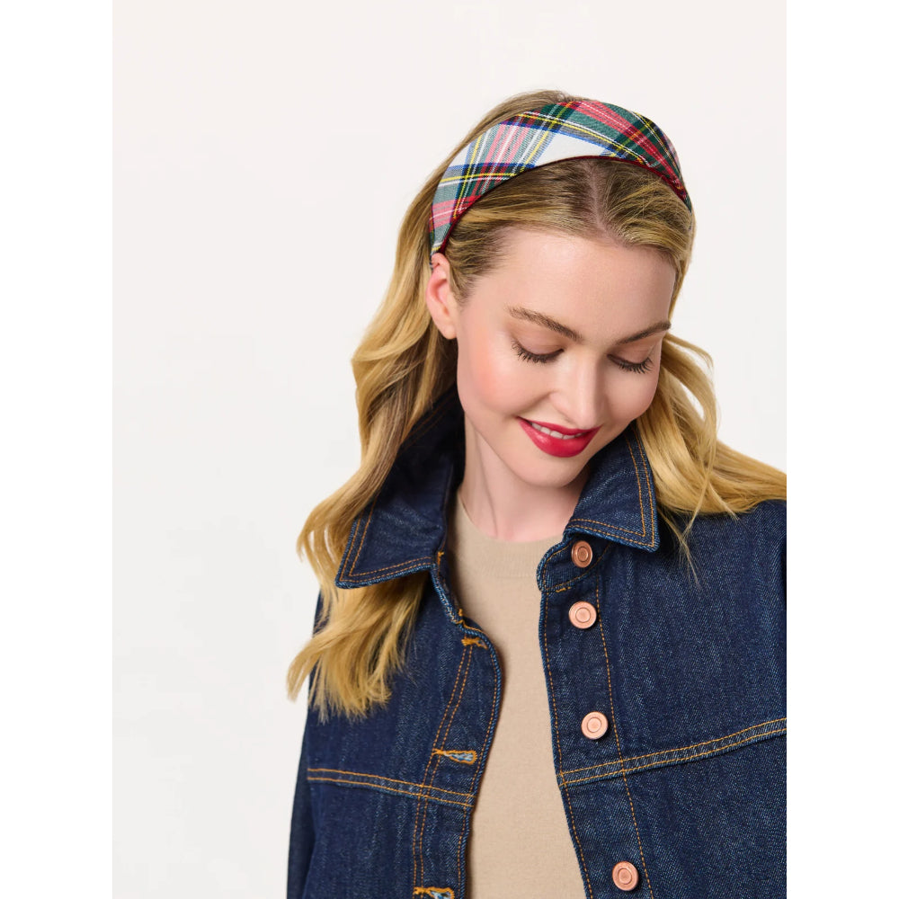 A woman wearing a multicolor plaid headband and a dark blue denim jacket over a beige top, photographed against a plain light background.