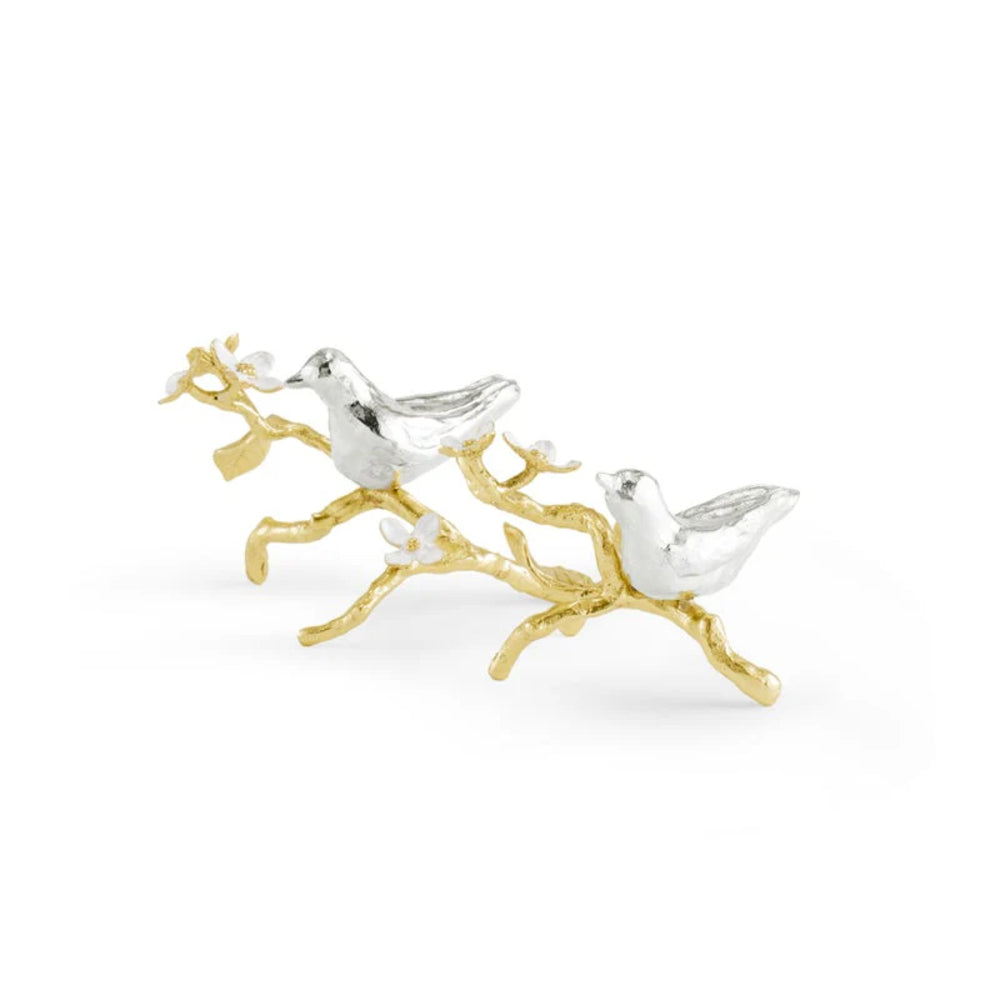 Silver and gold bird figurines on a branch against a white background