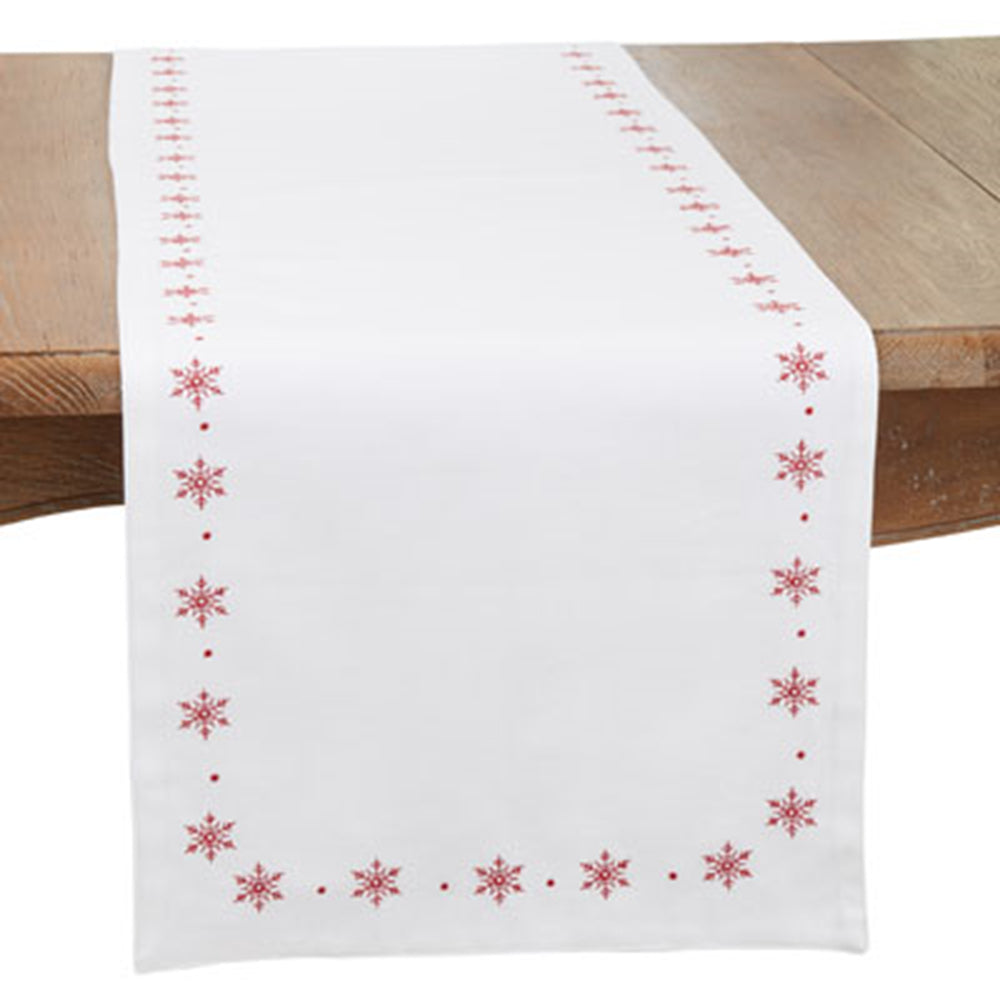 A white table runner with a red embroidered border of snowflakes and dots, draped over a wooden table.