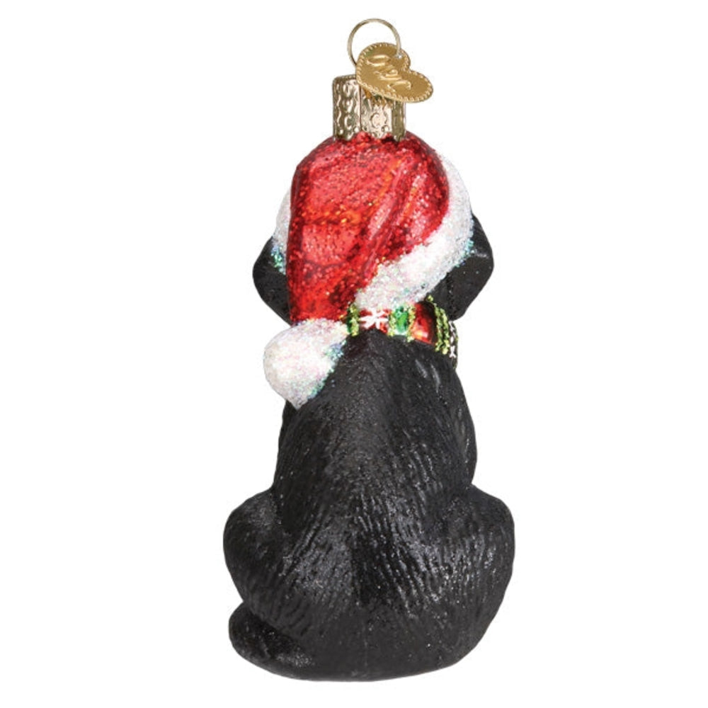 Glass ornament of a black dog wearing a red Santa hat on a white background
