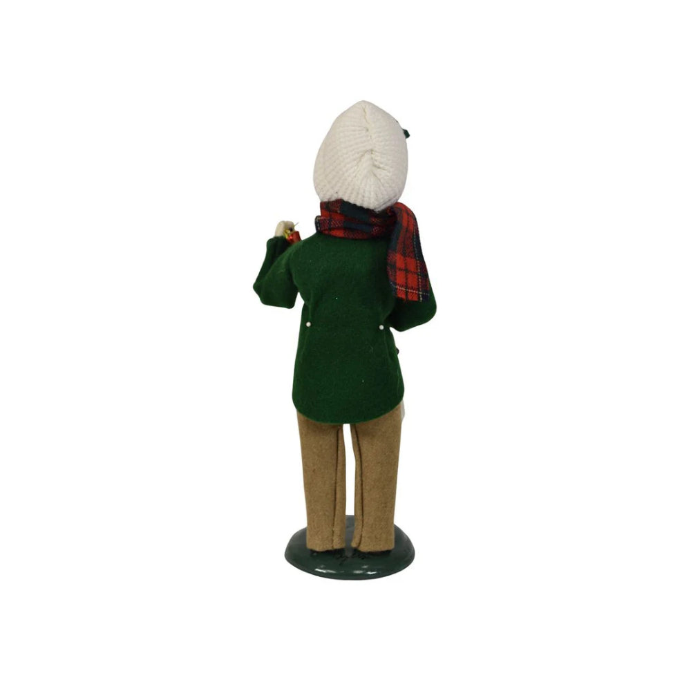 The back of a figurine of a caroling boy  wearing a green coat, plaid scarf, and white beanie on a white background