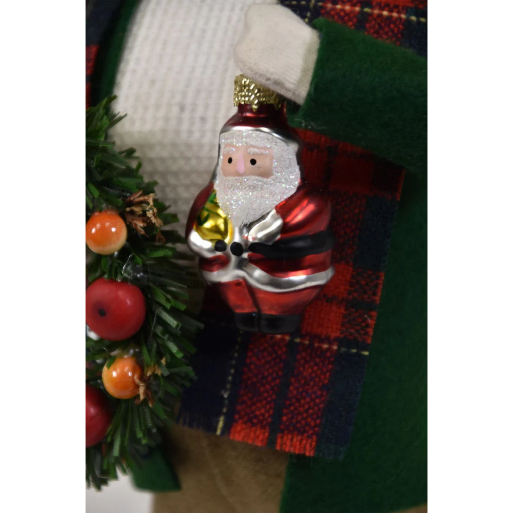 A close photo  of the santa ornament being held by a figurine of a caroling man 