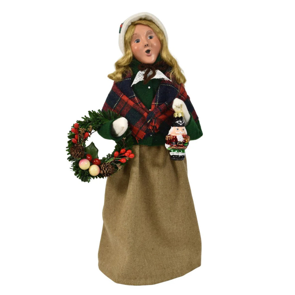 Colorful holiday decorative figurine of a  caroling woman holding a wreath and a small nutcracker ornanment  on a white background