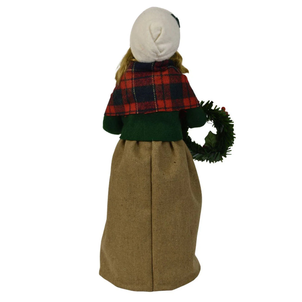 Back  photo of a colorful holiday decorative figurine of a  caroling woman holding a wreath and a small nutcracker ornanment  on a white background