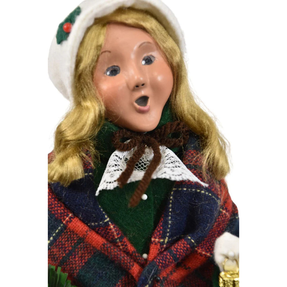 Close up photo of  the face of a colorful holiday decorative figurine of a caroling woman holding a wreath and a small nutcracker ornanment  on a white background