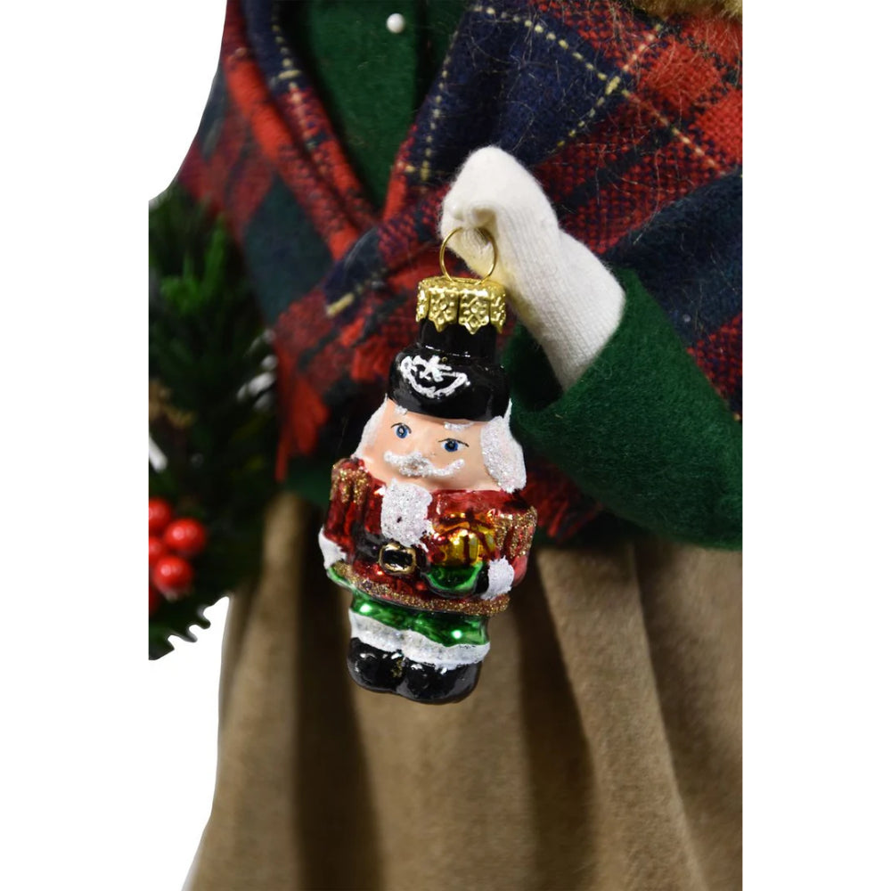 Christmas ornament of a nutcracker held by a person wearing a plaid coat.