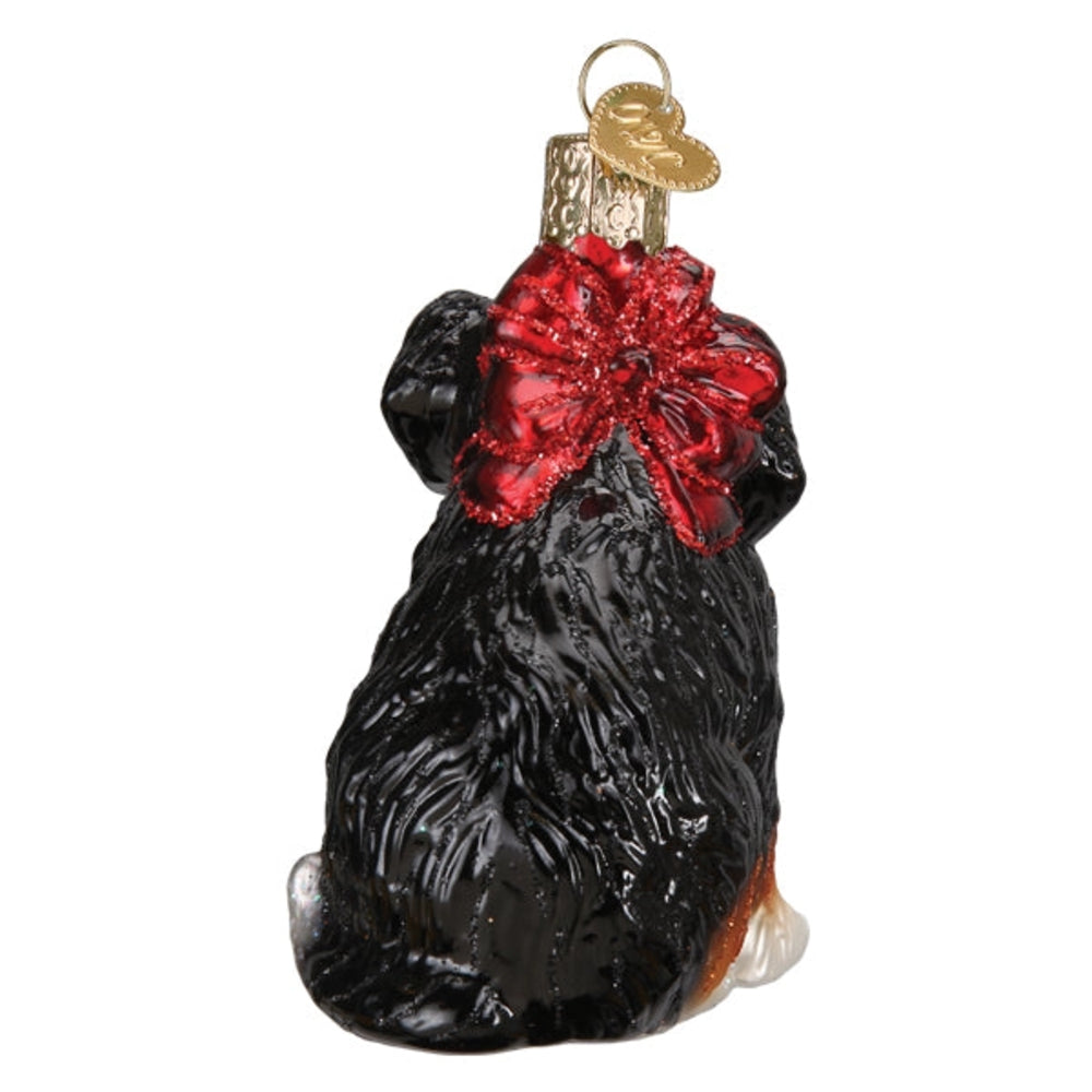 Glass ornament of a black dog with a red bow on a white background.