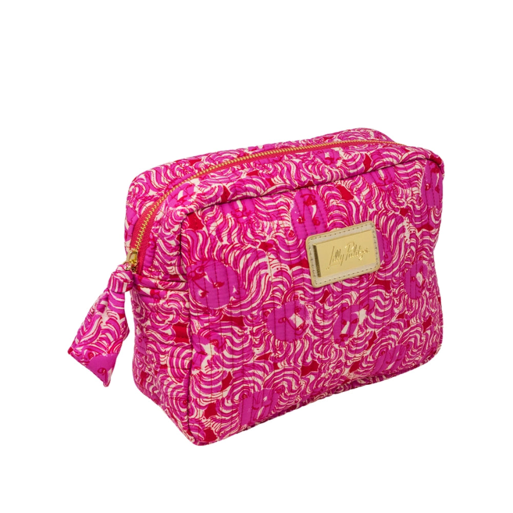 A bright pink cosmetic pouch with a white and red abstract pattern, featuring a gold-tone metal brand plaque on the front and a matching zipper pull.