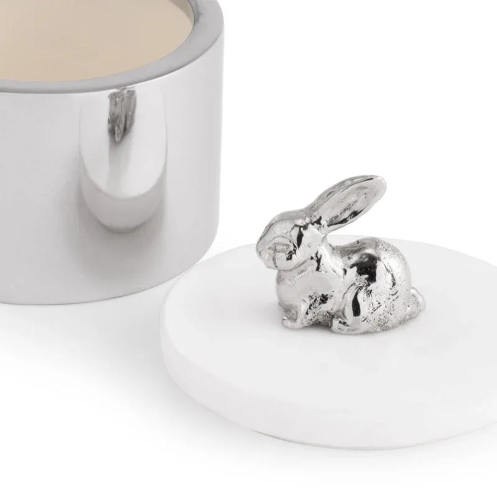 Silver rabbit-shaped object on a white surface with a white container in the background