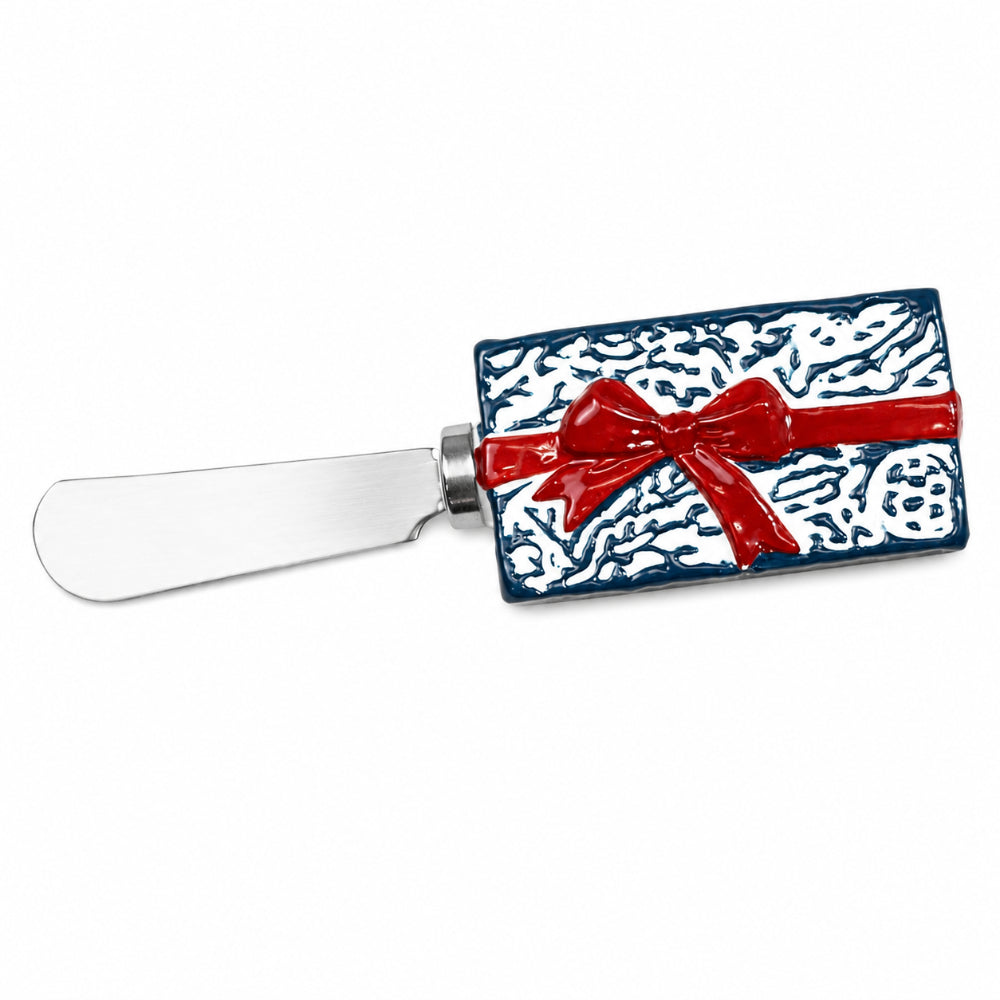 A decorative cheese knife with a silver metal blade and a handle sculpted to look like a wrapped gift box in white and navy blue with a red bow, shown on a plain white background.