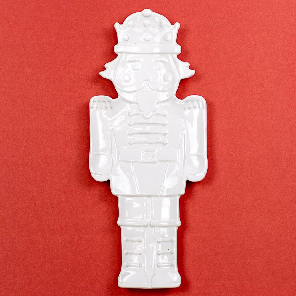 A white ceramic nutcracker figurine with a crown, displayed against a solid red background.