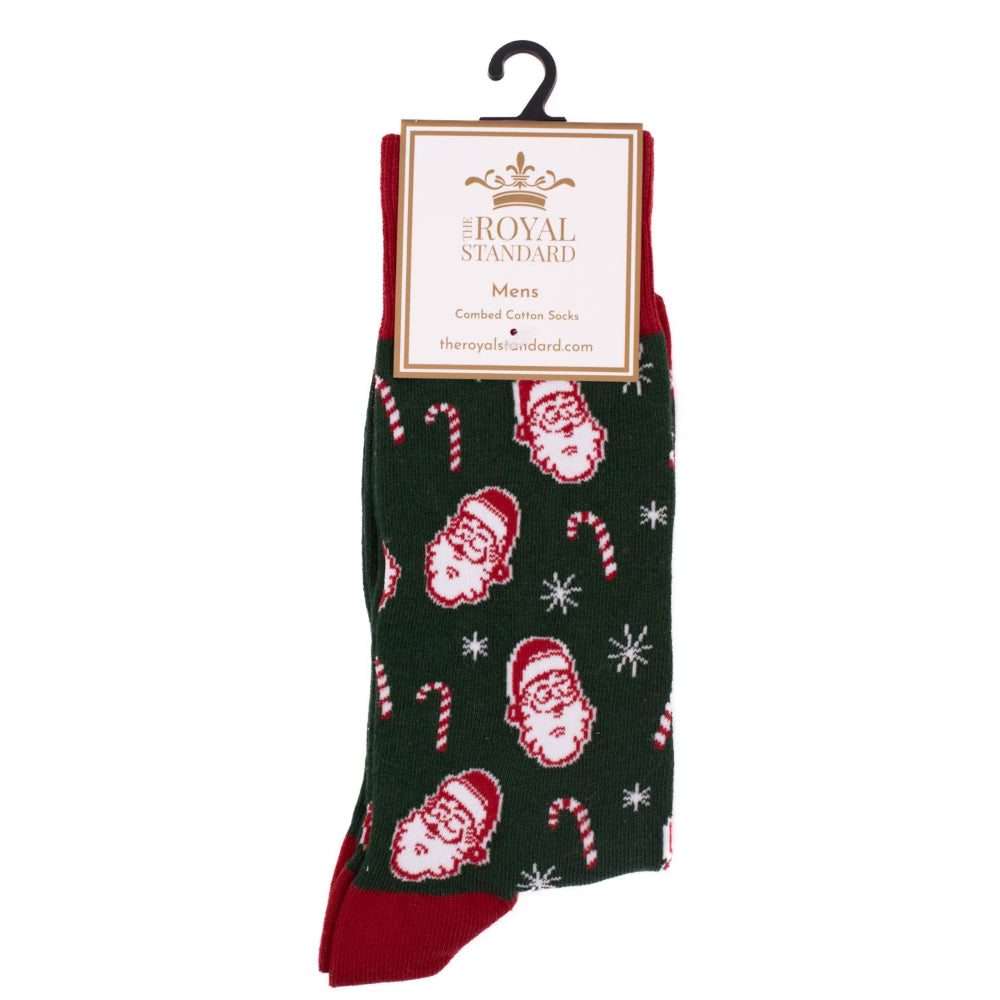 A pair of Christmas-themed men's combat socks by The Royal Standard, featuring a dark green background with red and white Santa Claus faces, candy canes, and snowflakes, with solid red heels and toes, hanging on a black hanger.