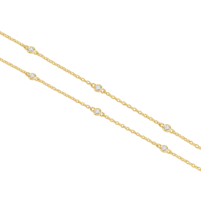A delicate gold chain necklace featuring small, spaced-out round bezel crystals, displayed diagonally on a white background