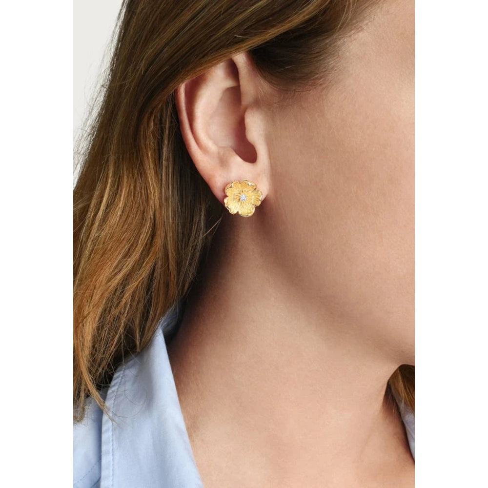 A close-up of a woman's ear wearing a small yellow flower stud earring with a tiny clear center stone.