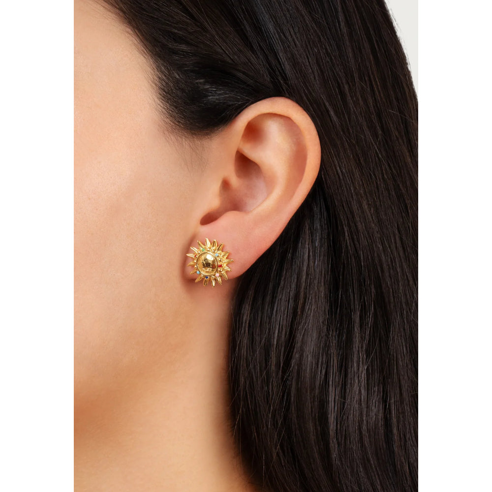 A close-up of a model's ear wearing a gold sunburst stud earring with a central pearl-like bead.