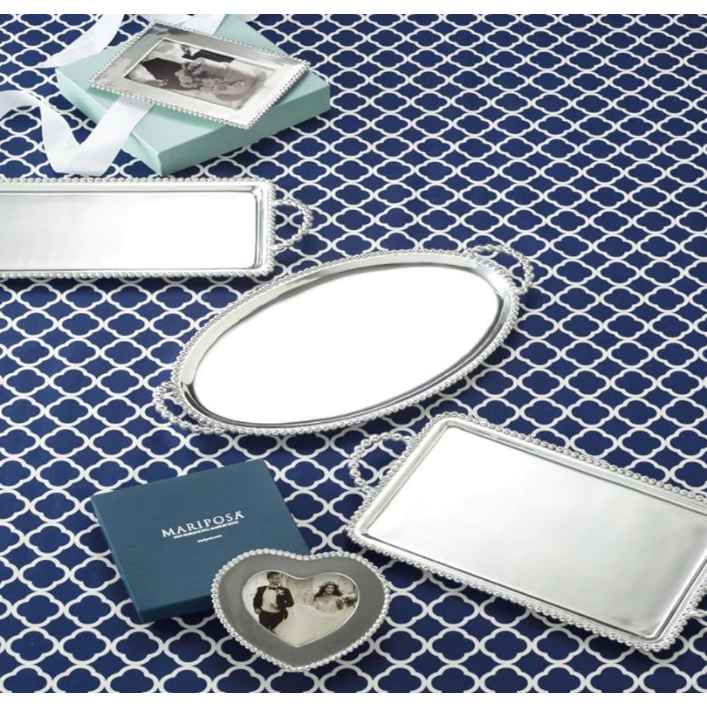 Decorative silver photo frame and and a oval and rectangle silver trays and a square mariposa boxes on a blue & white patterned surface