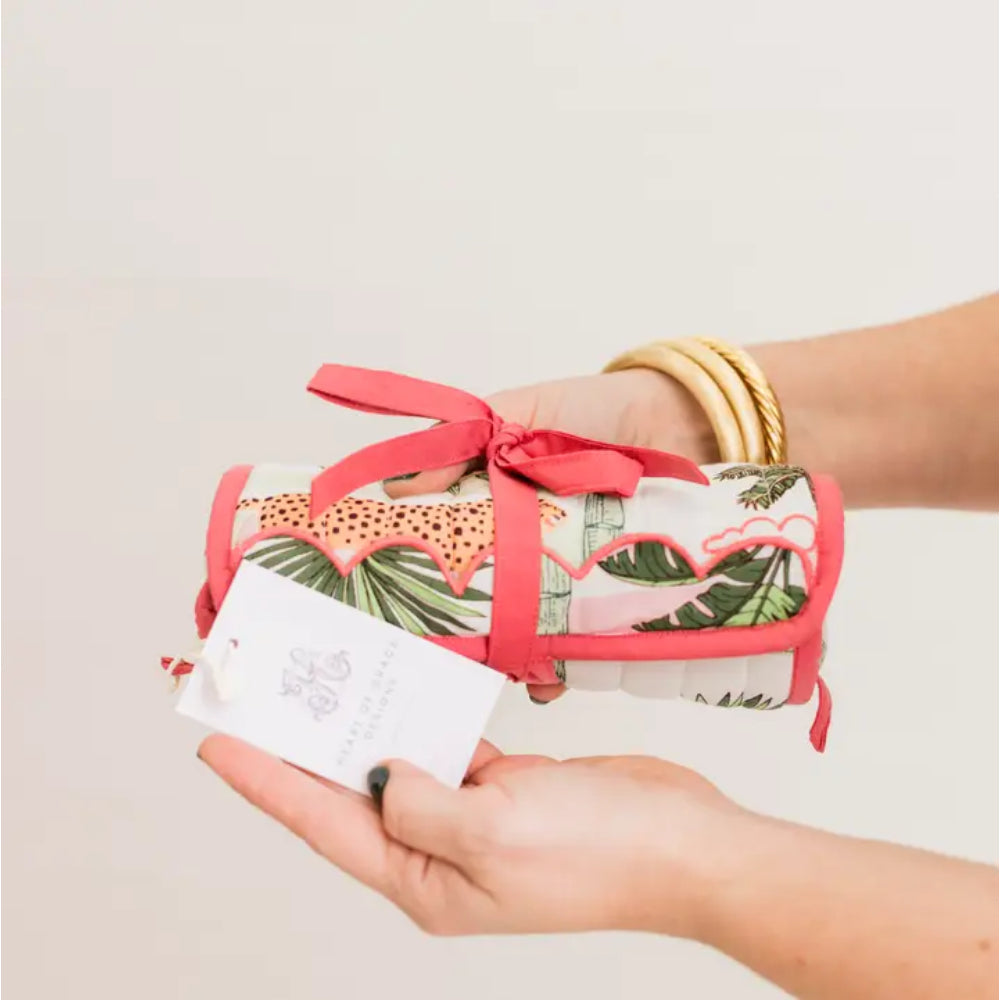 Hand holding a rolled-up item with a tropical leaf pattern and pink ribbon against a plain background