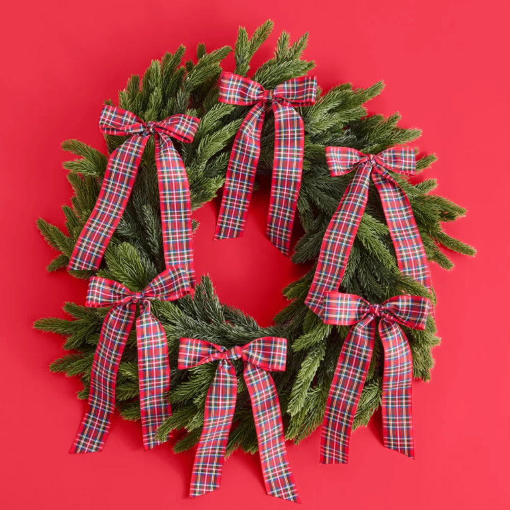A green pine wreath decorated with six red and green plaid ribbon bows, set against a solid red background.