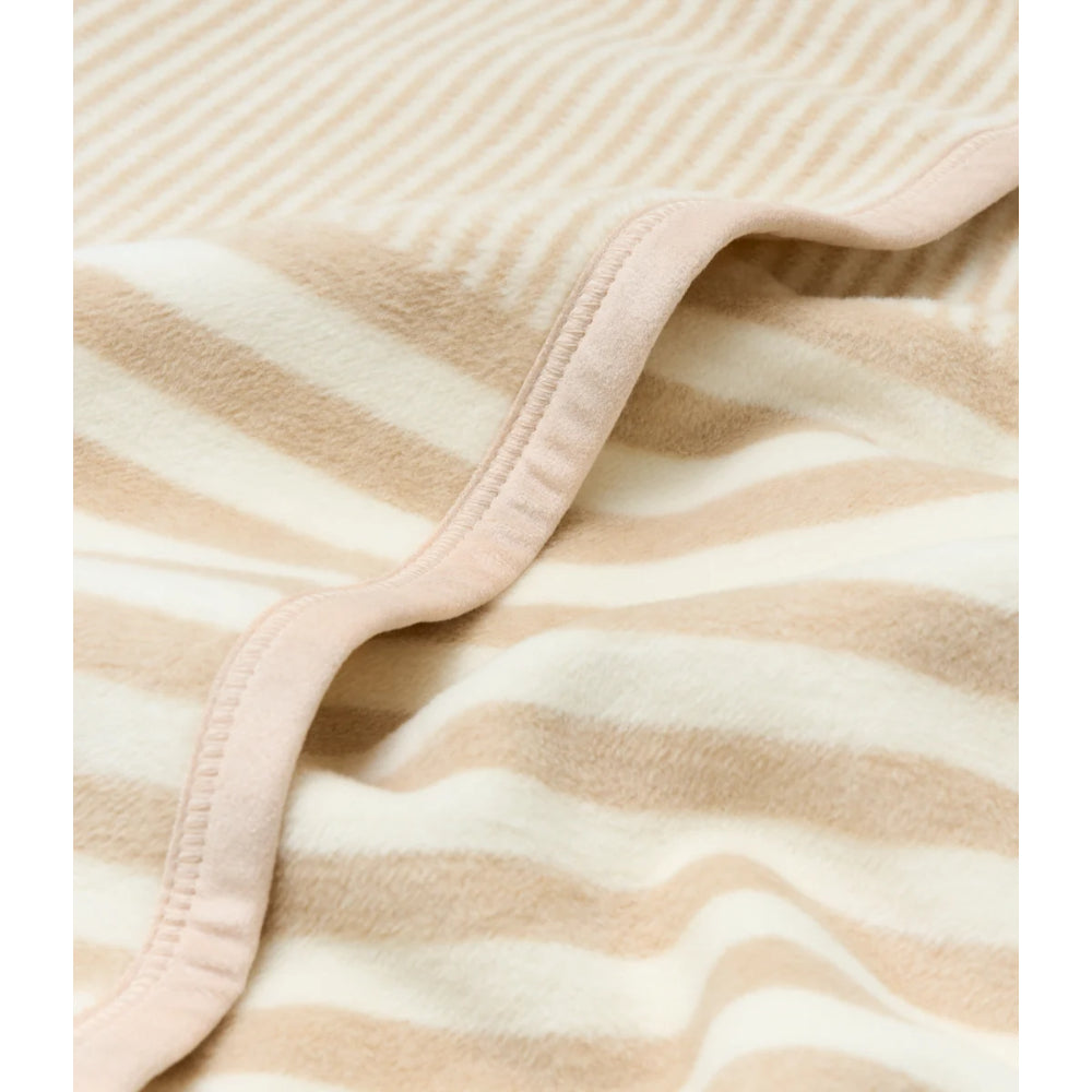 A close-up of a soft striped textile, likely a blanket or throw, with alternating beige and off-white horizontal stripes and a matching stitched border.