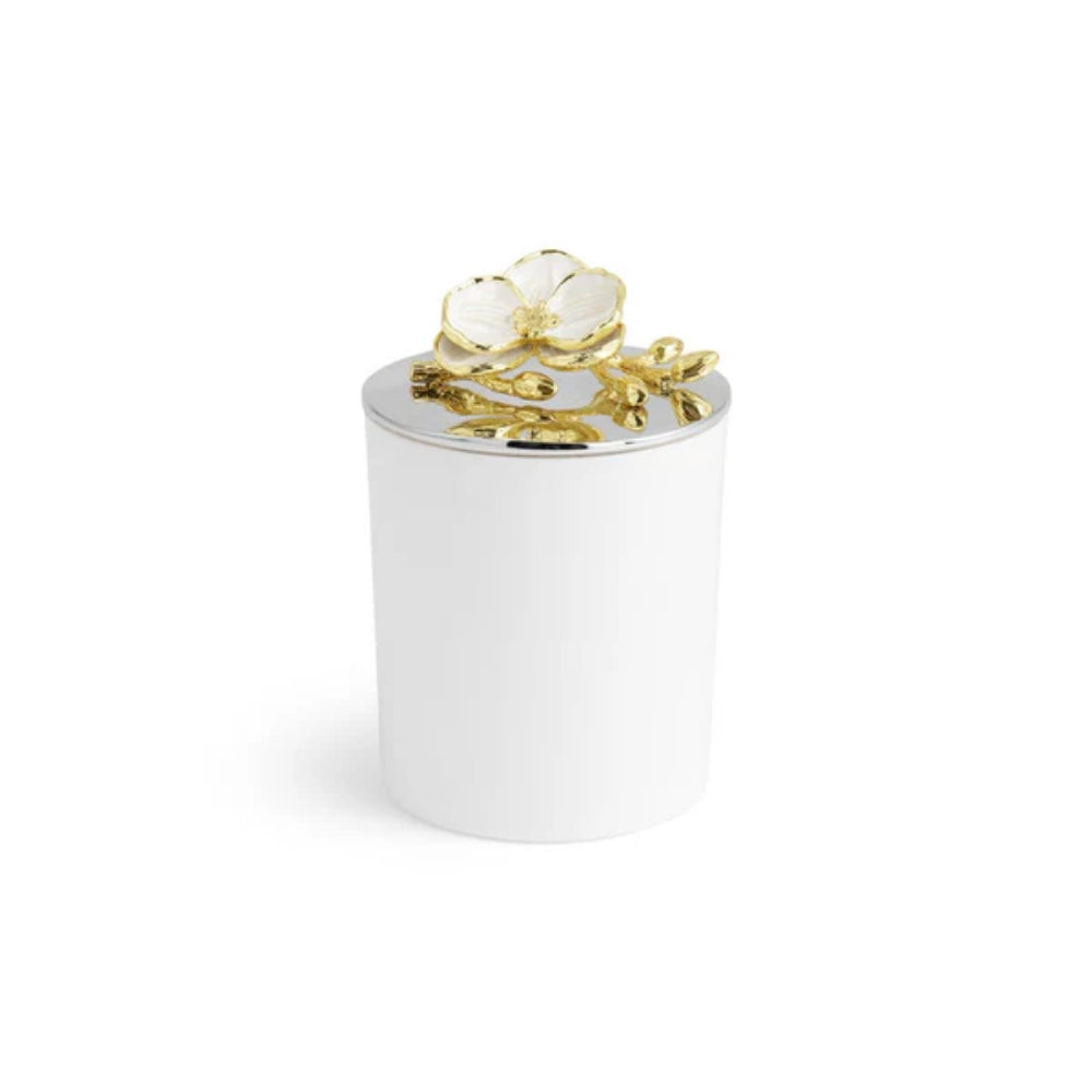 A small white candle with a white and gold floral design on a silverplated lid on a white backround