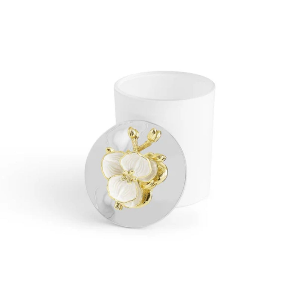 A small white candle with a white and gold floral design on a silverplated lid with the lid  off snd on the side of the candle on a white backround