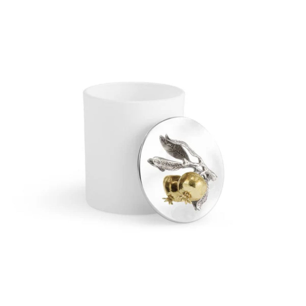 White candle with a gold and silver decorative pomegrante top a silverplated lid with lid of next to the candle on a white background