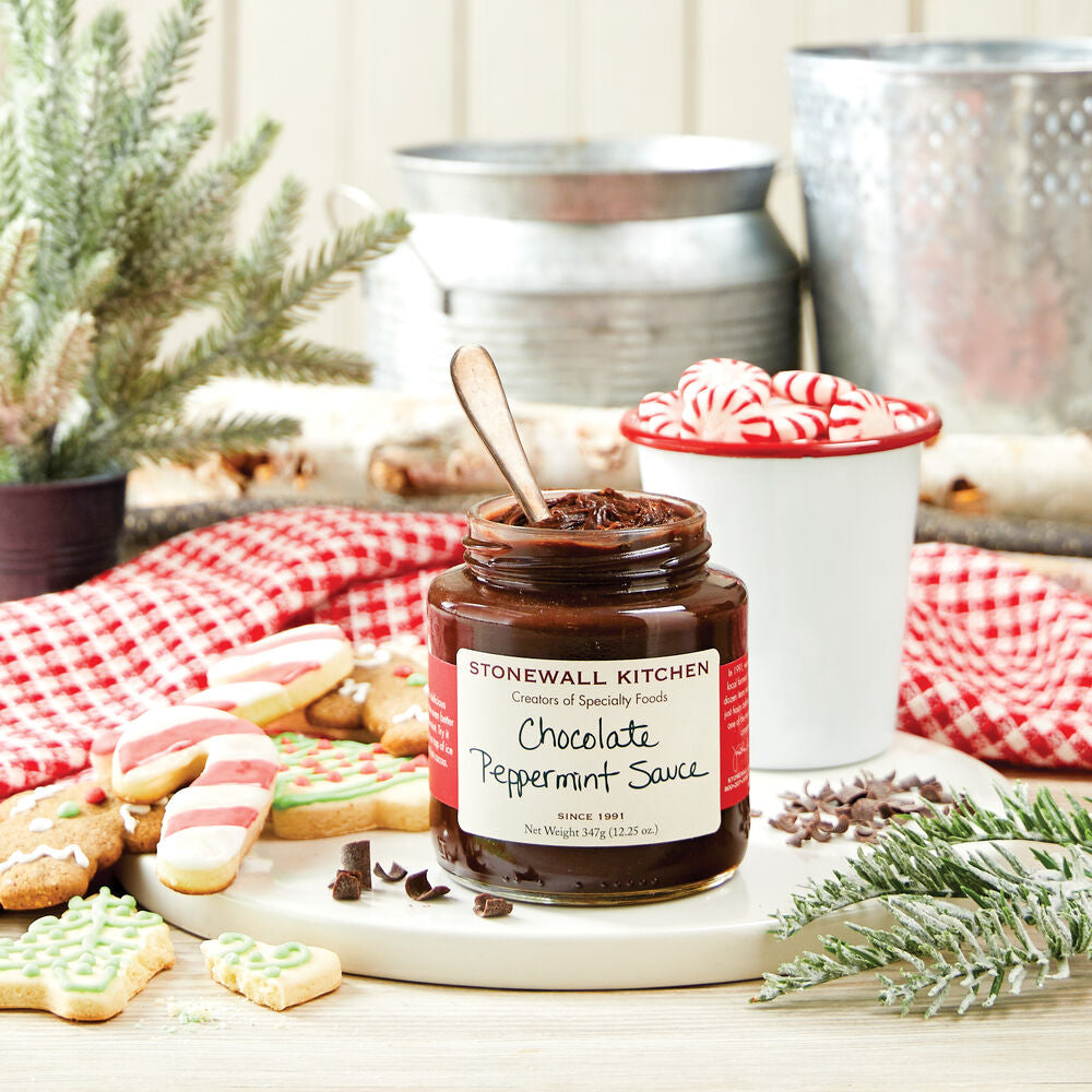 Jar of Stonewall Kitchen Chocolate Peppermint Sauce on a table with cookies and Christmas decorations.
