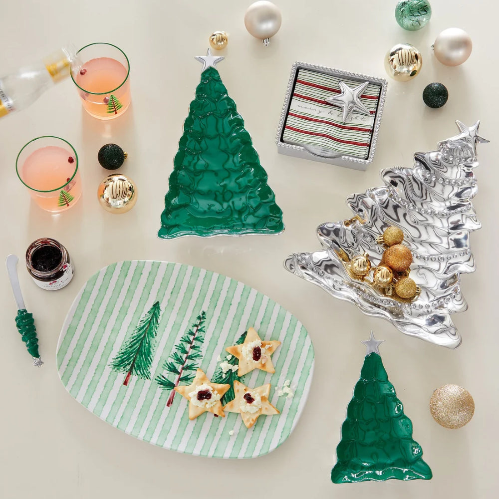 A small green tree candy dish with silver star on top with other tree themed holiday items and glasses on a on a white backround.