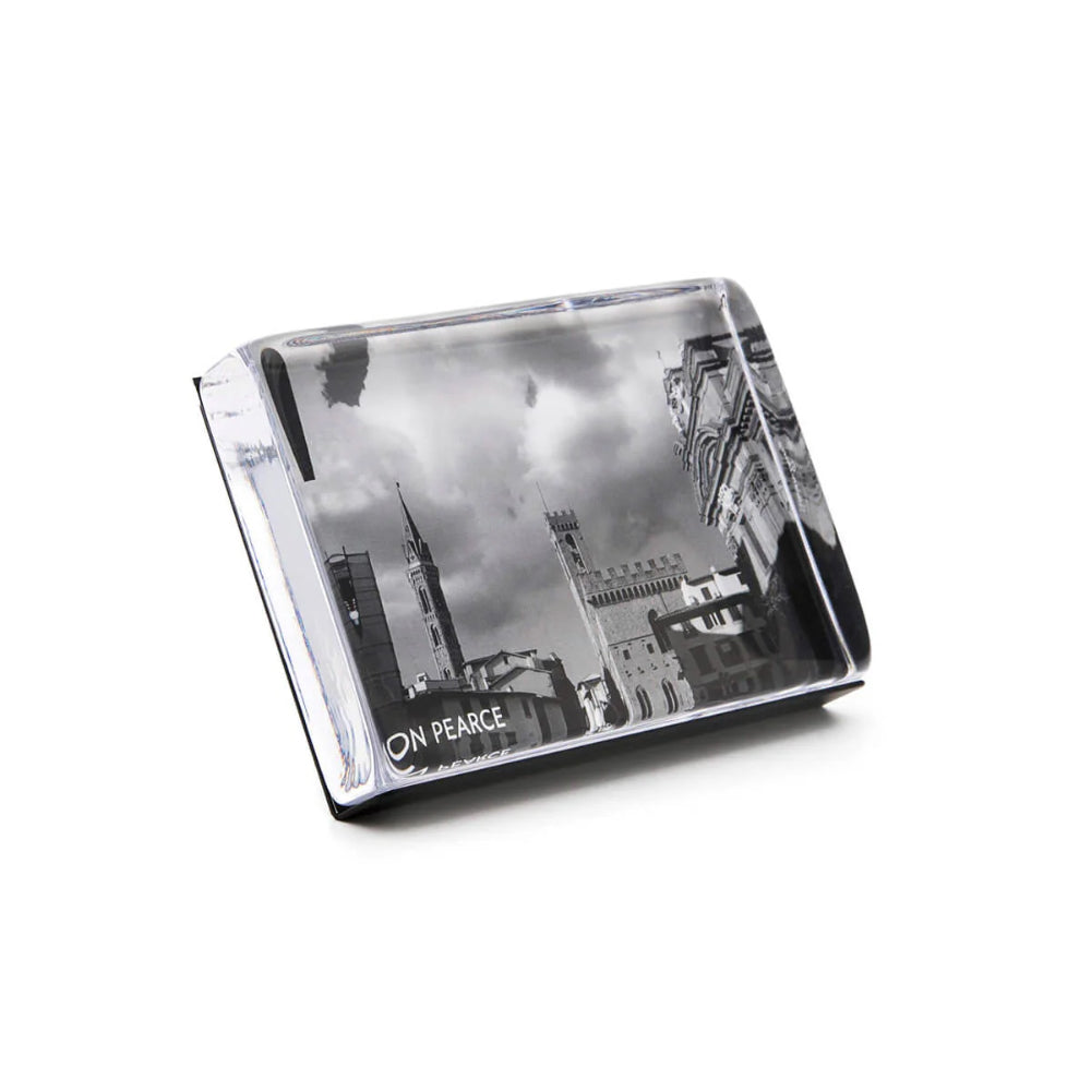 A angled side photo of a clear glass 4x6 photo block holding a 4x6 photo, featuring a reflection of buildings and clouds on its surface, displaying a memory or picture.