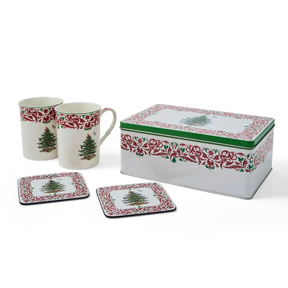A holiday-themed ceramic and metal tea or coffee set on a white background, including two mugs, two square coasters, and a rectangular tin with a lid. The white porcelain-style pieces are decorated with a red floral border and a green Christmas tree motif.