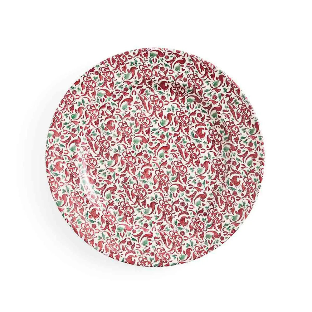 A round ceramic plate featuring an intricate hand-painted floral and paisley pattern in red and green on a white background, photographed from directly above on a clean white surface.