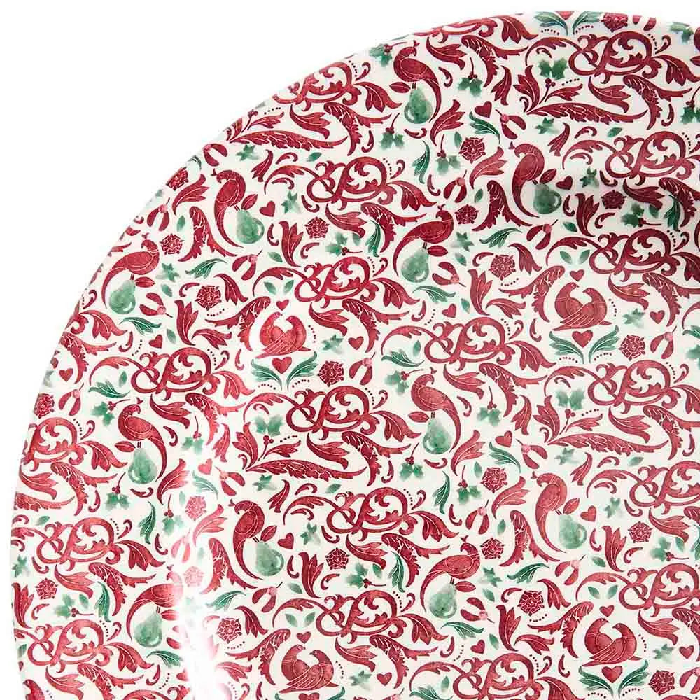 A close-up of a white ceramic plate featuring an intricate red and green floral and bird pattern, with a glossy finish and a white background visible in the upper left corner.