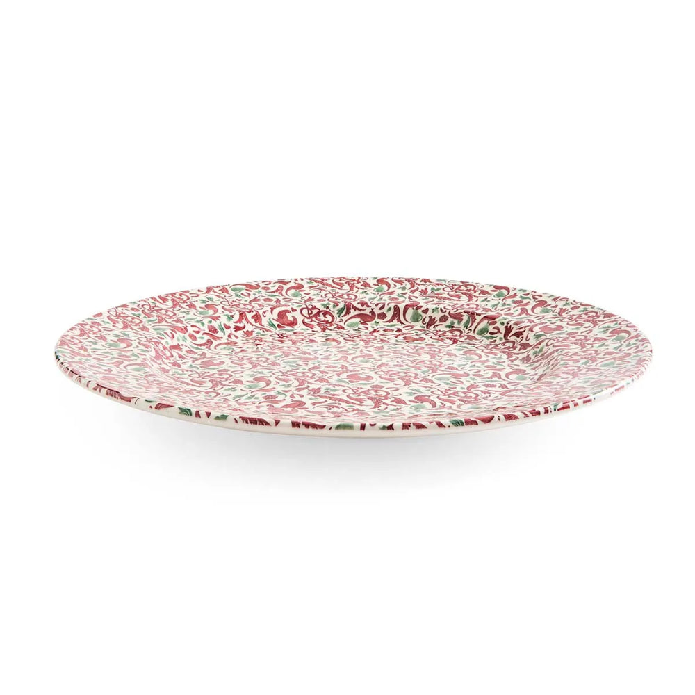 A round ceramic serving platter with a dense red, green, and white floral pattern, shown from a direct overhead angle on a white background.