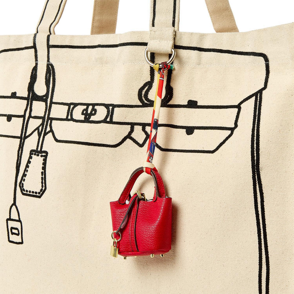 Red handbag keychain with a strap attached to a beige tote bag with black line art.