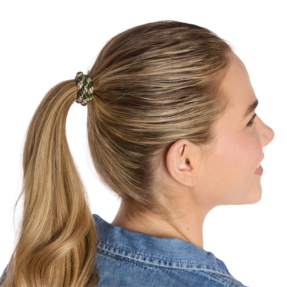 Woman with blonde hair in a ponytail wearing a denim jacket and useing the green hair ties on a white background.