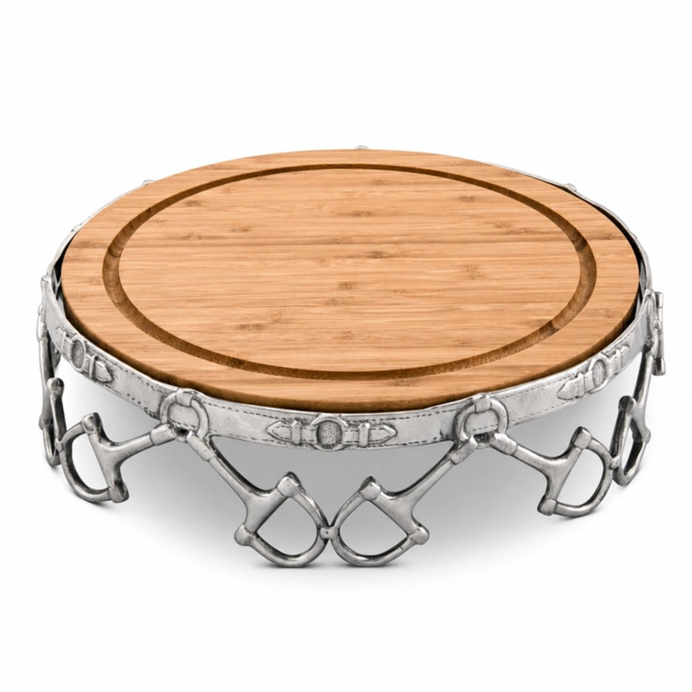 A round wooden cutting board with a silver metal rim decorated with horsebit hardware, shown on a white background.
