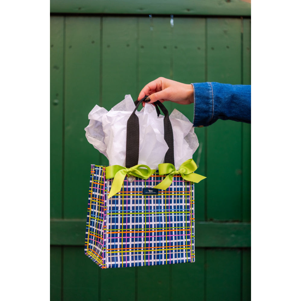 Hand holding a colorful plaid gift bag with a green ribbon against a green wooden background
