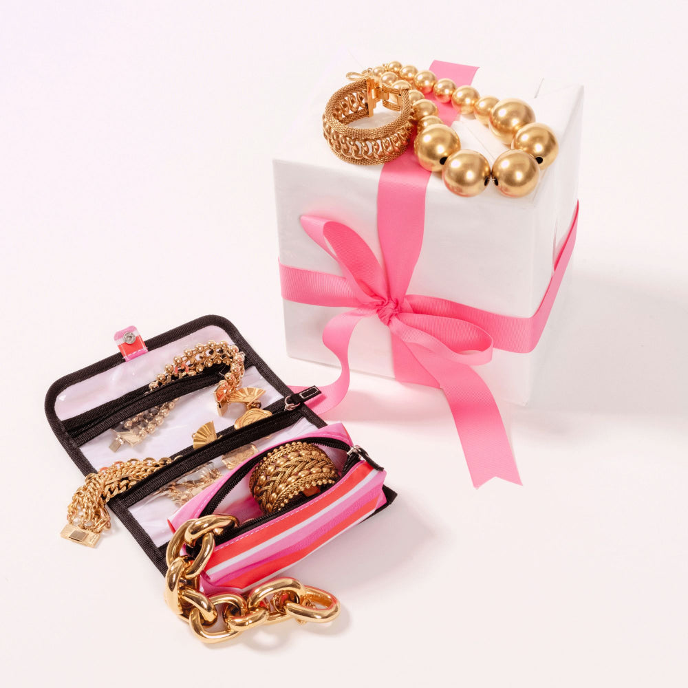Gold jewelry set displayed on a white gift box with a pink ribbon, alongside an open black jewelry organizer containing matching gold chain, bracelet, and beaded bracelet pieces.