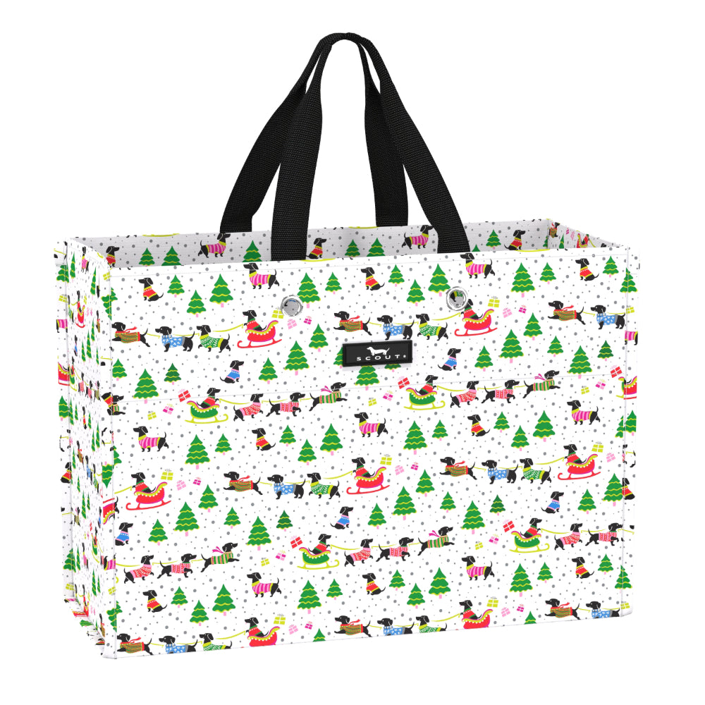 A white gift bag with black handles, featuring a festive Christmas pattern of dachshunds in sleds, green pine trees, and snowflakes. A small black brand label reading 'pup & play' is visible on the front.
