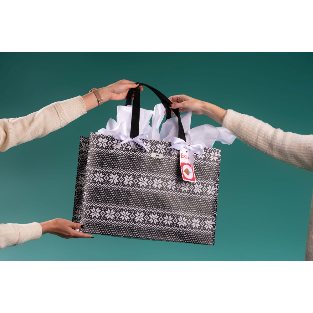 A large black and white patterned gift bag with white tissue paper and a red-and-white price tag, held by three person hands against a teal background.