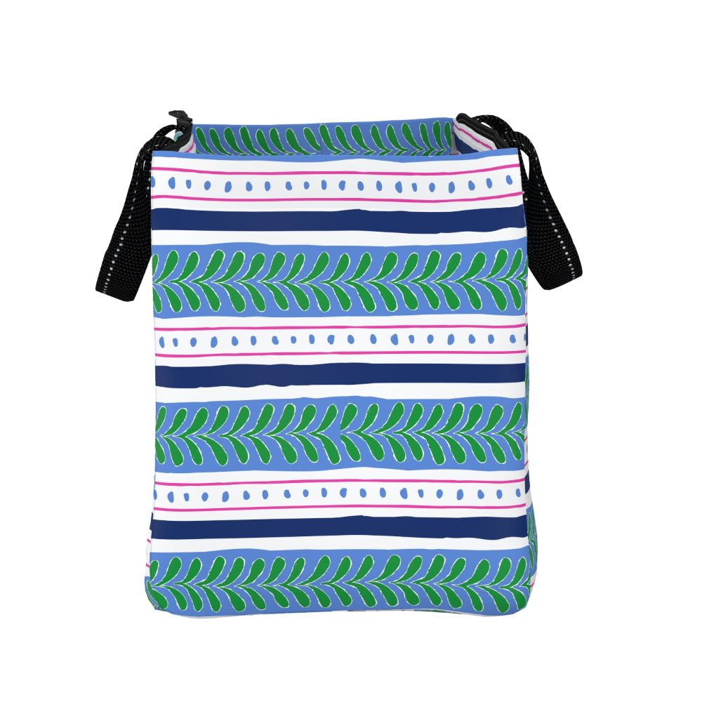 A rectangular crossbody bag with a colorful horizontal pattern featuring green leafy motifs, navy blue stripes, and light blue bands on a white background. It has black shoulder straps with white stitching.