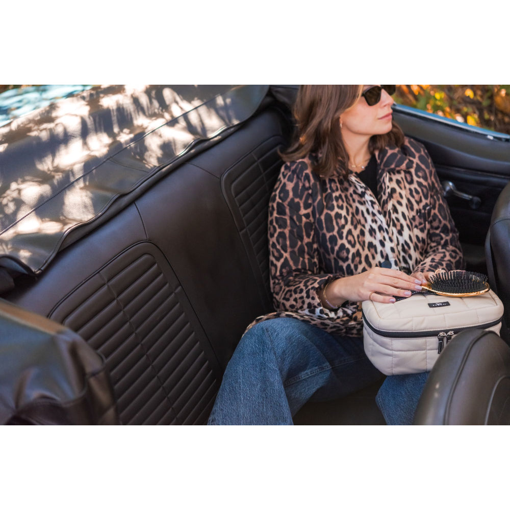 Woman in leopard print coat sitting in a car with a hairbrush and pouch.