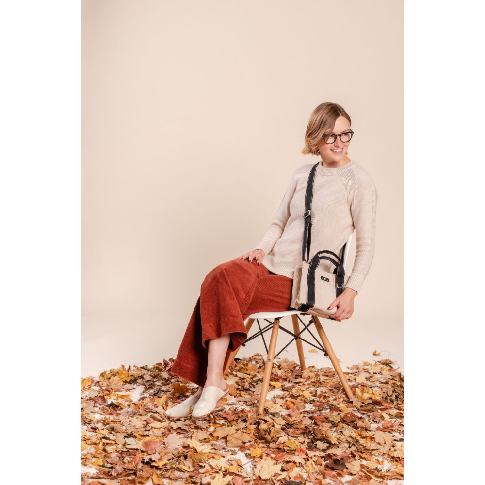 Woman sitting on a chair surrounded by autumn leaves against a beige background