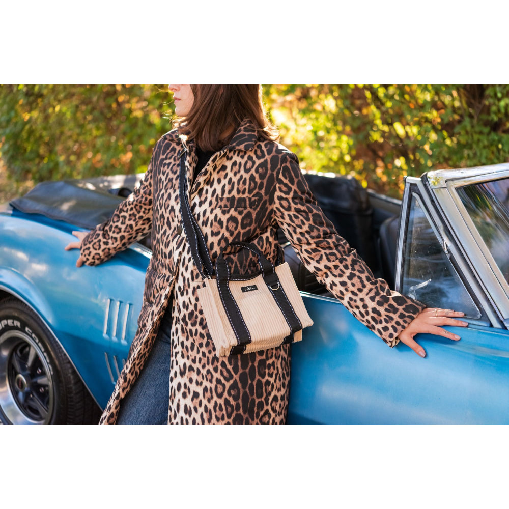 Person in leopard print coat with beige handbag standing next to a blue convertible car.