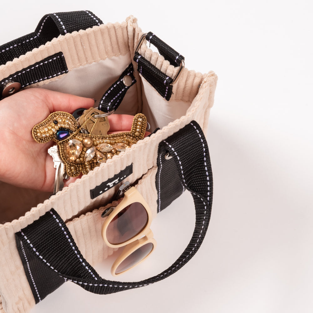 Hand holding a decorative keychain with a dog design over an open beige handbag.