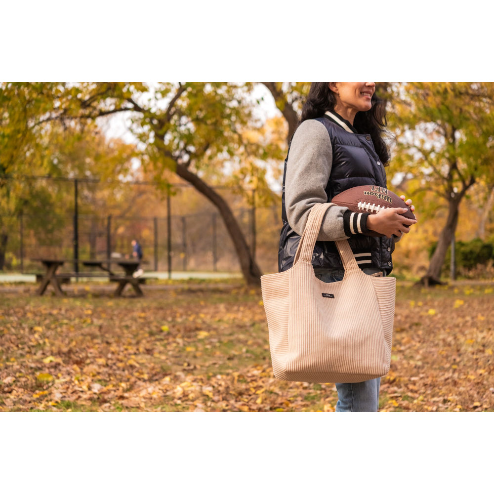 Person holding a beige tote bag and a football in an autumn park setting