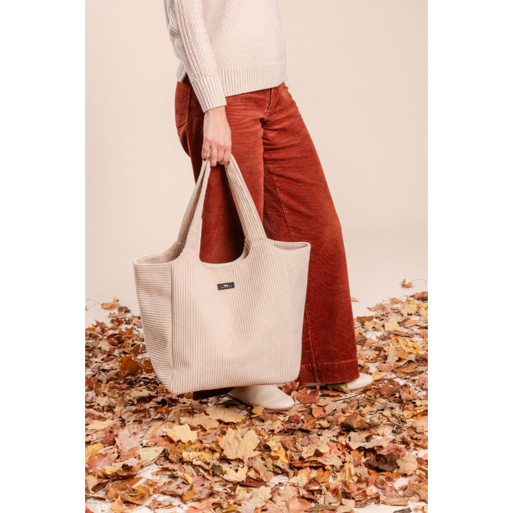 Person holding a beige tote bag on a background of autumn leaves