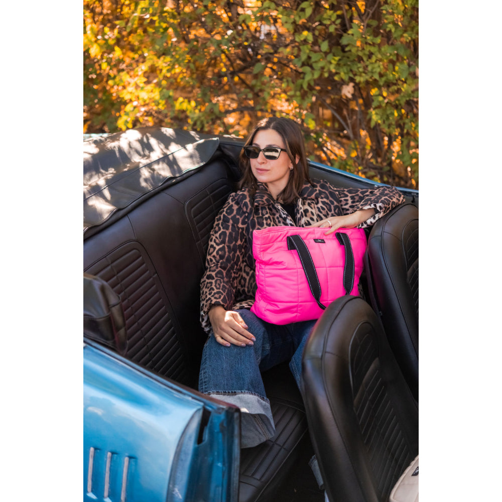 Woman sitting in a car with a pink bag, surrounded by autumn foliage.