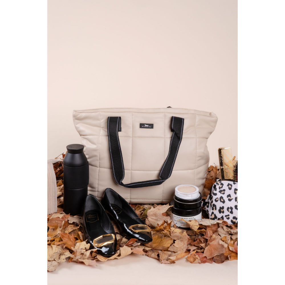 Beige tote bag with black accents, black shoes, and a black water bottle on a surface with autumn leaves.